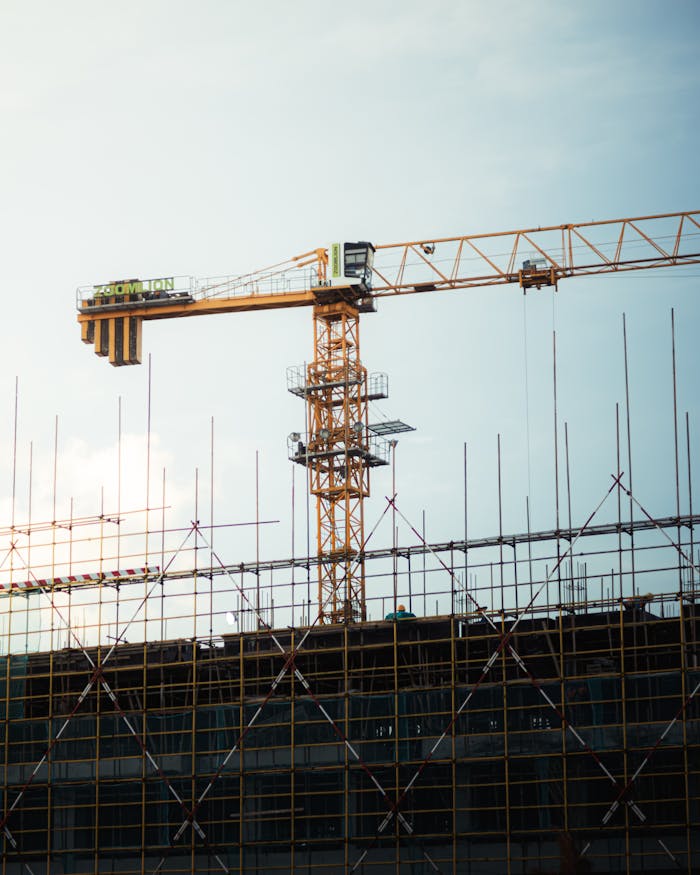 A construction site with cranes and metal framework silhouetted against a sunset sky.